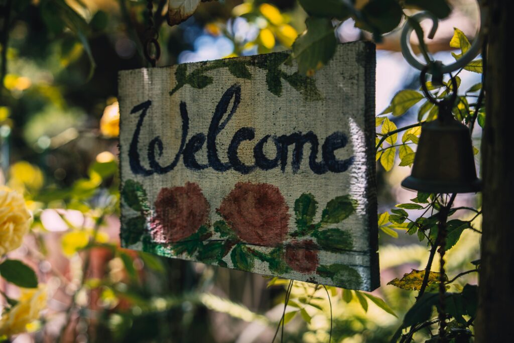 A charming hand-painted welcome sign with roses hanging in a sunny garden setting.